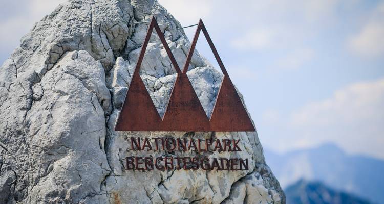 Rostfarbenes Metallschild mit der Aufschrift "Nationalpark Berchtesgaden" auf einem rauen Felsvorsprung angebracht.