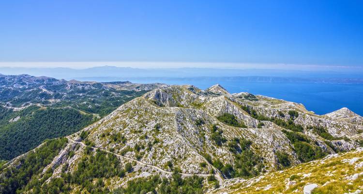 Unas montañas cársticas enormes se extienden hacia el Mar Adriático bajo un cielo azul cristalino.