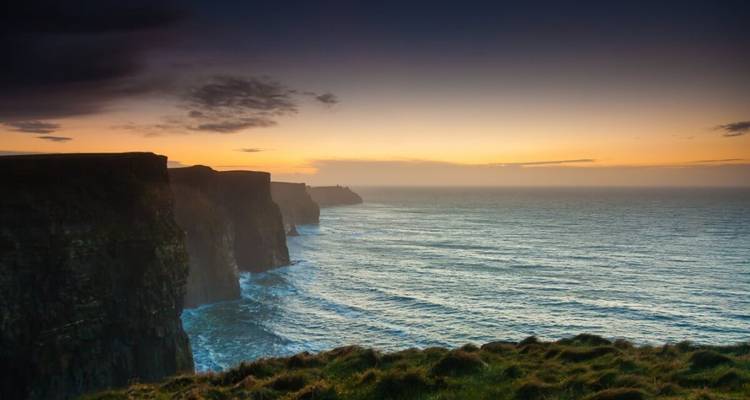 Falaises surplombant l'océan au coucher du soleil avec un premier plan herbeux.