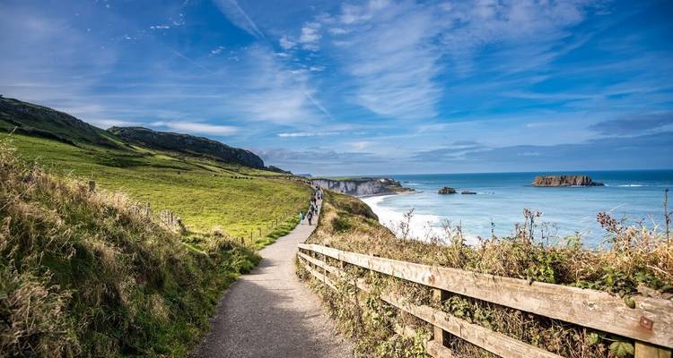 Sentier de promenade le long d'une côte herbeuse avec des personnes au loin.