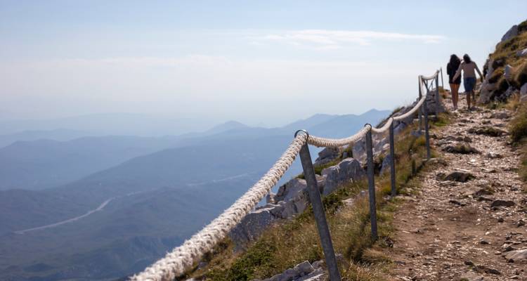 Excursionistas en un sendero de montaña con barandilla de cuerda.