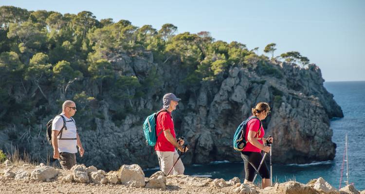 Trois randonneurs marchant le long d'un sentier rocheux côtier.