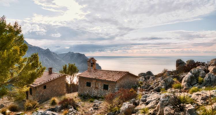 Maisons en pierre rustiques surplombant la mer avec des montagnes.