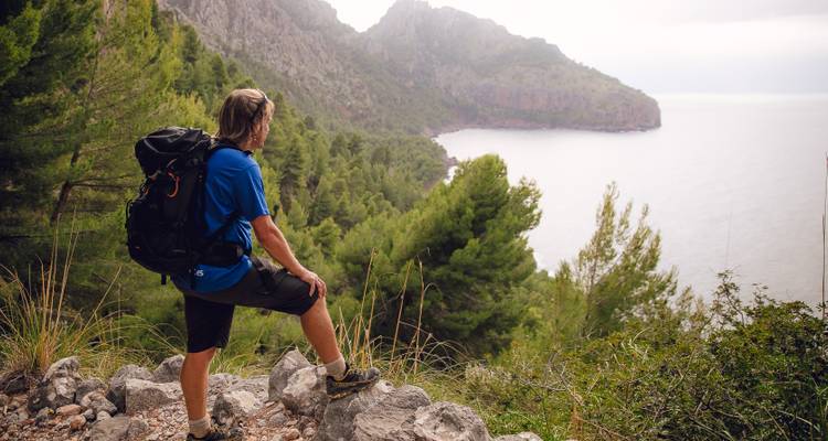Personne faisant de la randonnée avec un sac à dos contemplant une vue côtière.