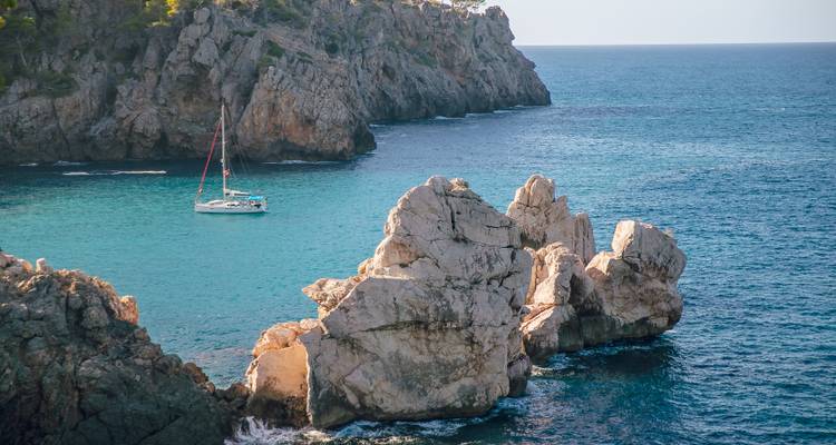 Paysage côtier avec de l'eau bleue claire et un voilier.