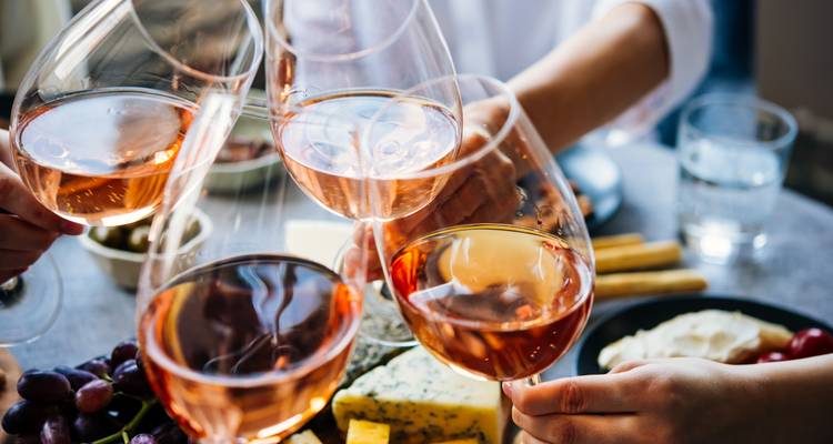Mensen die glazen roséwijn laten klinken aan een tafel met verschillende voedingsmiddelen.