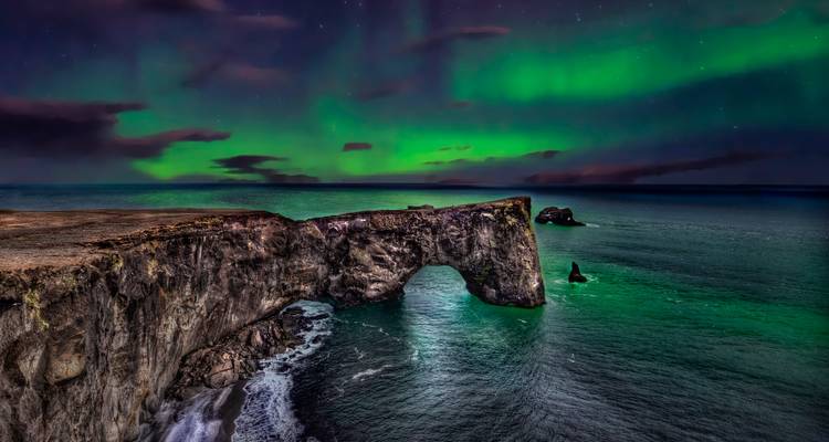 Nordlichter über einem Felsbogen am Meer.