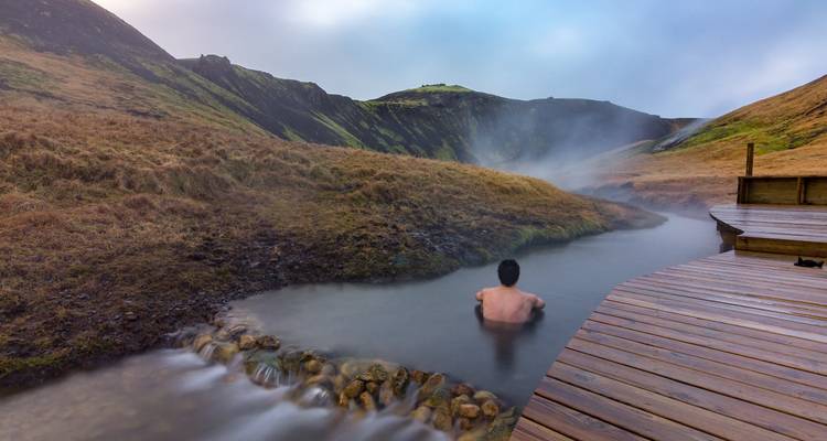 Person entspannt sich in einer natürlichen heißen Quelle, umgeben von Bergen.