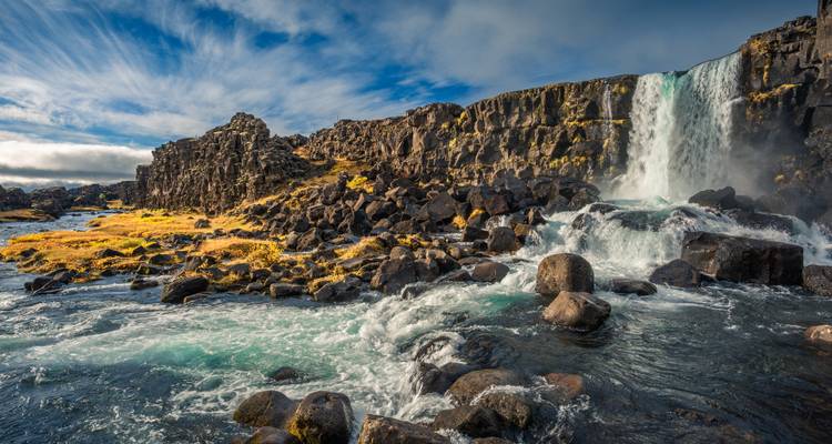 Wasserfall, der über Felsen hinabstürzt, mit bewölktem Himmel.