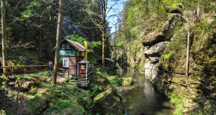 Eine rustikale Hütte an einer ruhigen Flussschlucht, umgeben von üppigem Wald.
