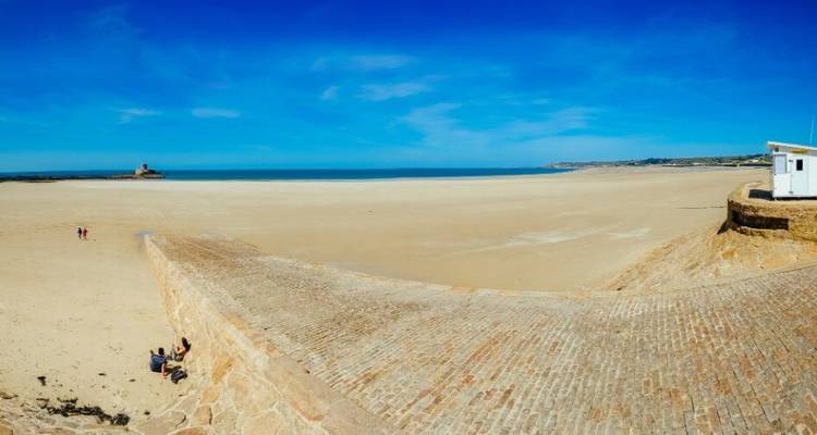 Large plage de sable avec une petite fortification et un ciel bleu.