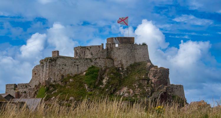 Château fortifié avec un drapeau au sommet, entouré d'herbe.