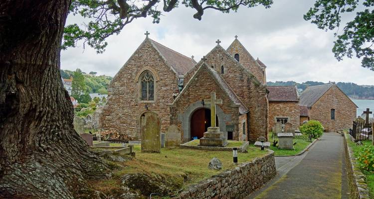 Église de pierre historique avec un cimetière, située dans un paysage rural paisible.
