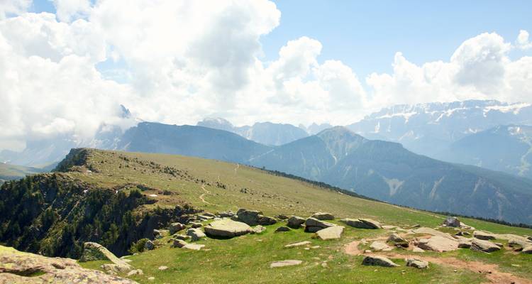Vue panoramique de montagne avec des collines herbeuses et un ciel nuageux.