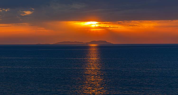 Zonsondergangzicht over de zee met het silhouet van een ver eiland.