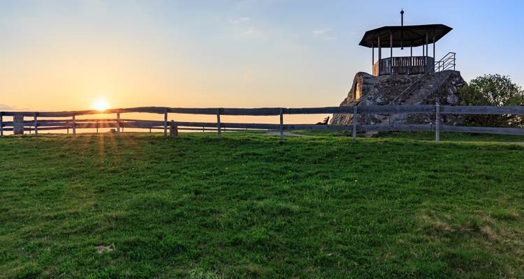 Vista del atardecer desde una plataforma de observación con vista a un campo cubierto de hierba.