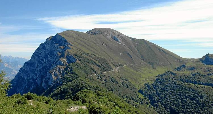 Crête de montagne verte et accidentée sous un ciel strié avec un sentier sinueux visible sur la pente.