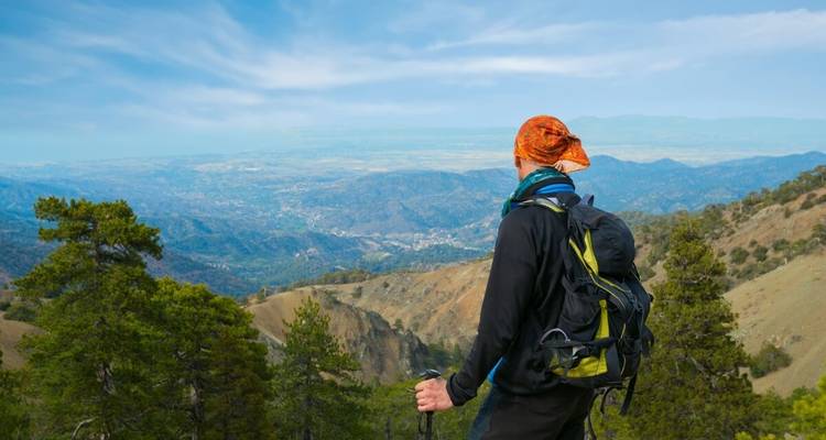 Ein Rucksacktourist blickt über ein weitläufiges Bergtal und entfernte Ebenen in Zypern.