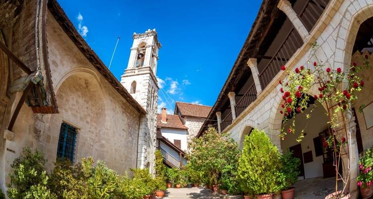 Innenhof eines Steinenklosters mit Glockenturm, Bögen und blühenden Rosen unter blauem Himmel.