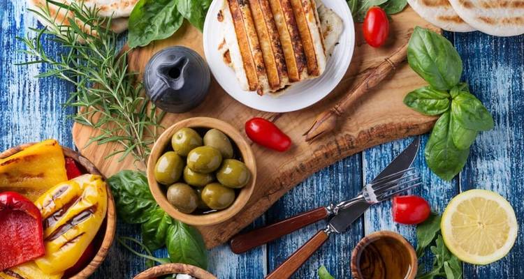 Farbenfrohe zypriotische Meze-Auswahl mit Halloumi, Oliven, Kräutern und Zitrone auf rustikalem Tisch.