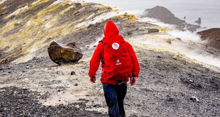 Person in roter Jacke, die durch eine Vulkanlandschaft in Italien wandelt.