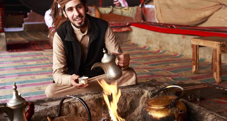 Homme en tenue traditionnelle servant du café dans une tente.