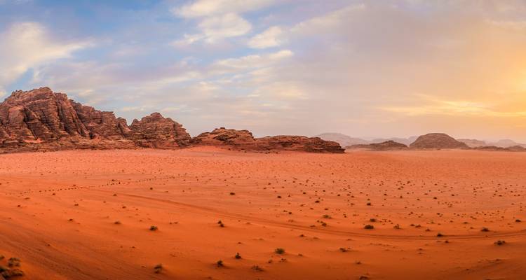 Vast desert landscape with red sand dunes and rocky formations.
