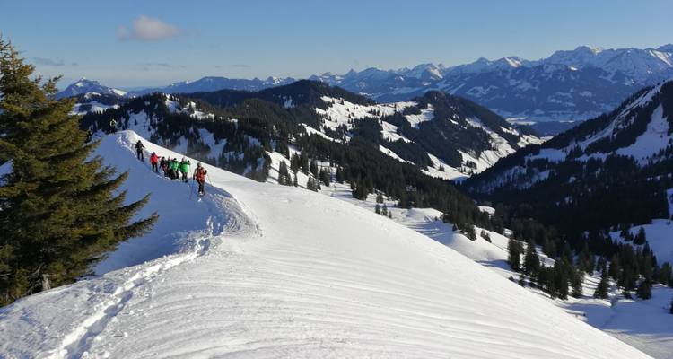 A line of hikers walking along a snowy ridge with expansive views.