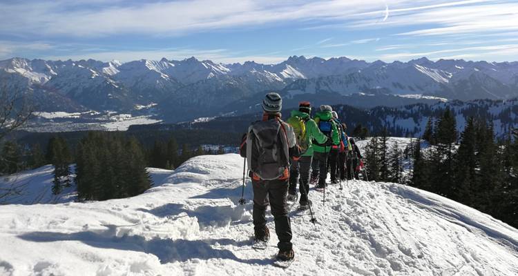 A group of people hiking over a snowy ridge with mountainous views.