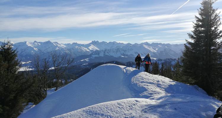 Two people on a snowy hilltop with expansive mountain views.