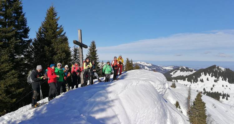 A group of people gathered around a cross on a snowy summit.