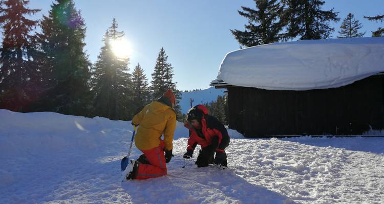 Two people preparing equipment in the snow with a wooden cabin nearby.