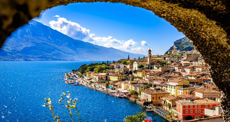 Eine malerische Stadt am Gardasee ist von einem Steinbogen mit blauen Gewässern und Bergen dahinter gerahmt.