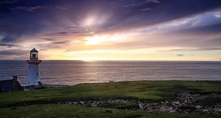 Phare dans un endroit pittoresque au bord de la mer au coucher du soleil.