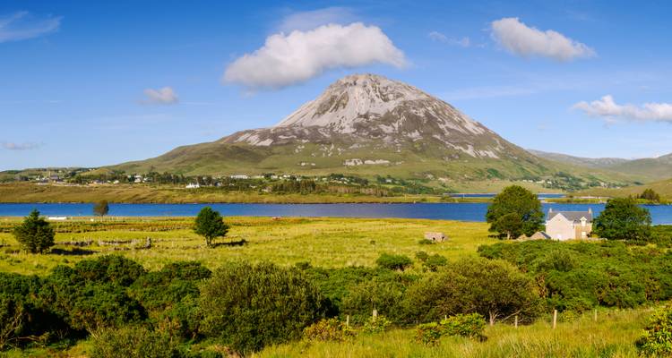 View of a solitary mountain with a lake and green fields.