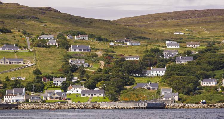 Small coastal Irish village of white cottages scattered on green hillsides above the sea.