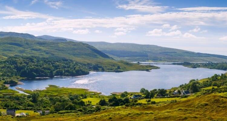 Lac pittoresque entouré de collines ondulantes et de maisons dispersées.