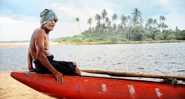 Oudere man met een kano op een zanderige rivieroever.