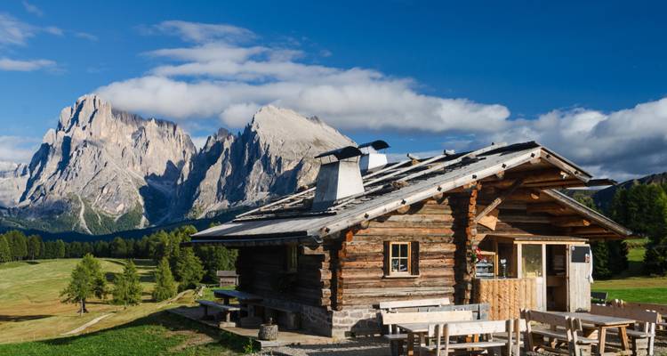 Rustic cabin on a mountain meadow with dramatic peaks.