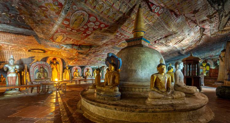 Intérieur d'un temple rupestre avec des statues et des peintures ornées.