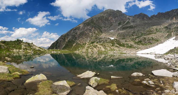 A serene alpine lake reflecting snow-dotted mountains under a clear blue sky.