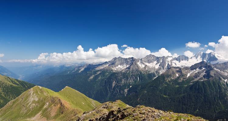 Panoramic view of rugged mountain peaks with clear sky and green valleys.