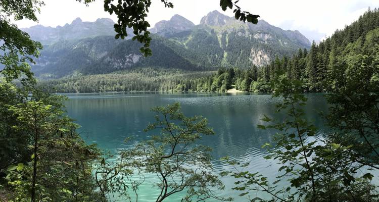 Calm lake surrounded by lush forest and mountains under a partially cloudy sky.