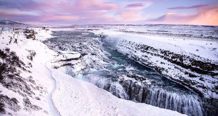 Schneebedeckte Klippen und eisiges Wasser stürzen unter rosa Morgenröte-Wolken in den tosenden Gullfoss-Wasserfall.