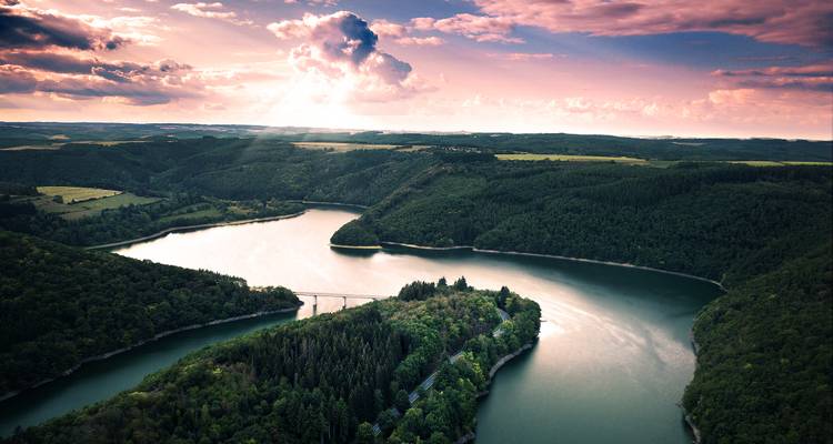 Ein malerischer Blick auf einen Fluss, der sich bei Sonnenuntergang durch die bewaldeten Hügel schlängelt.