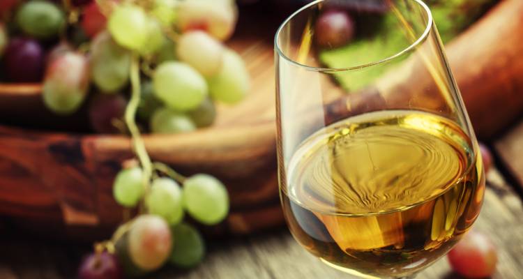 Nahaufnahme eines Weinglases mit Trauben im Hintergrund.