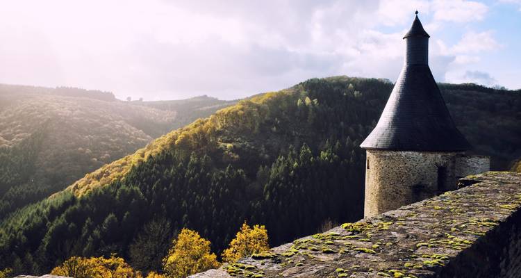 Mittelalterlicher Burgturm mit malerischen bewaldeten Hügeln als Kulisse.
