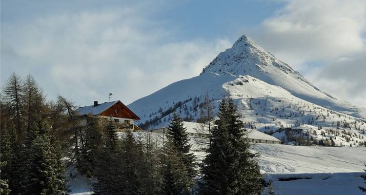 Un paysage de montagne enneigé avec une cabane en bois et des arbres.
