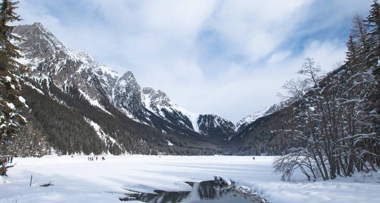 Gefrorener See umgeben von schneebedeckten Bergen und Bäumen.