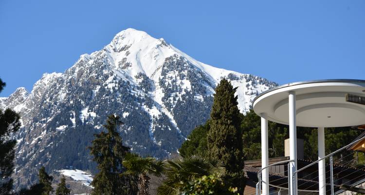 Dramatic snow-covered mountain peak rising behind modern terrace architecture against a clear blue sky.